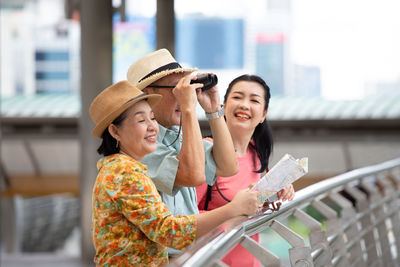 Happy young woman holding umbrella while standing on railing