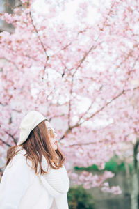 Low angle view of woman standing by pink flowering tree