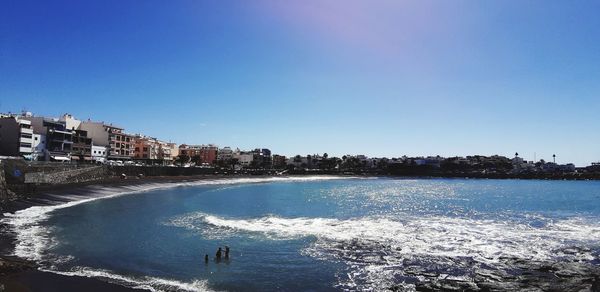 Scenic view of sea by buildings against clear blue sky