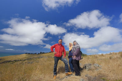 Portrait of family standing on mountain against blue sky during sunny day
