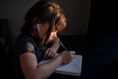 Rear view of girl sitting on book at home