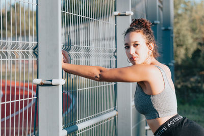 Portrait of young woman standing by fence