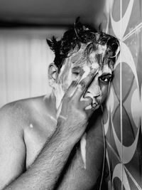 Portrait of shirtless young man with soap sud bathing in bathroom