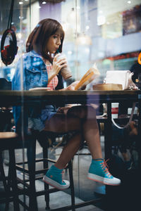 Young woman with book drinking iced coffee on restaurant table
