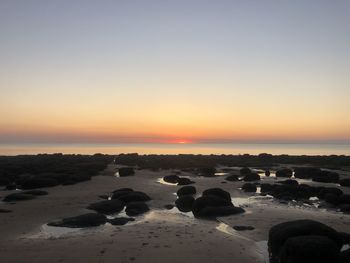 Rocks on beach against sky during sunset