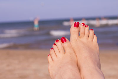 Low section of woman with red nail polish at beach