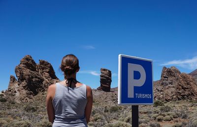 Rear view of woman standing by parking sign at desert against sky