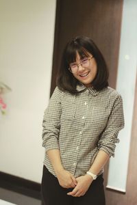 Portrait of smiling young woman standing against wall