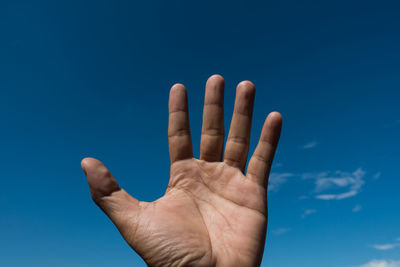 Cropped hand of man gesturing against blue sky