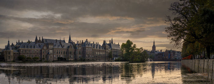 Buildings by river against sky during sunset