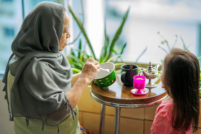 Senior malaysian muslim woman stay at home. sitting at the balcony apartment while having breakfast.