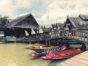 Boats moored on river by houses against sky