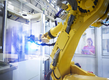 Technician operating yellow robotic arm through tablet pc in factory