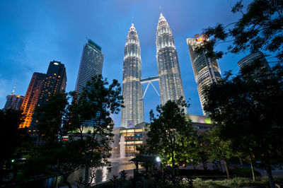 Low angle view of trees and illuminated skyscrapers