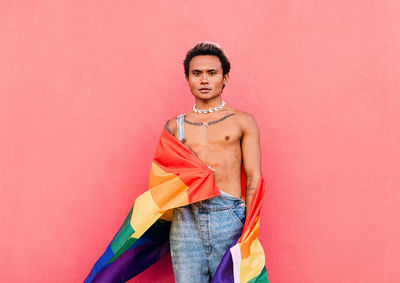 Portrait of man holding rainbow flag standing in front of pink wall