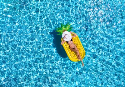 Full length of woman in bikini lying on inflatable raft floating over swimming pool