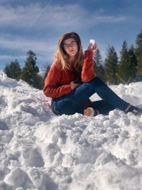 Portrait of woman sitting on snow field against sky