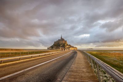 Road passing through building against cloudy sky