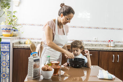 Mother preparing food in container by son on table