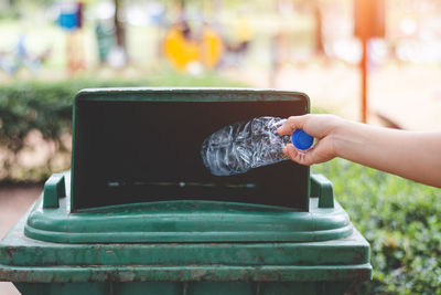 Cropped hand throwing bottle in garbage can