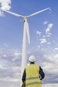 Engineer wearing reflective clothing looking at tall wind turbine