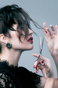 Woman cutting hair with scissors against gray background