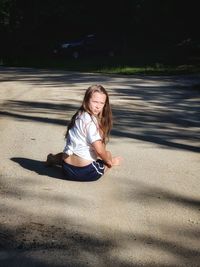 Portrait of girl sitting on road during sunny day