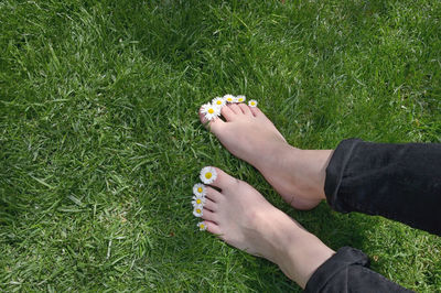 Low section of woman with flowers standing on grassy field