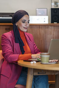 Young woman using phone while sitting on table