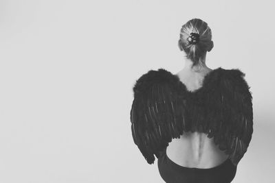 Rear view of woman with angel wings sitting against white background