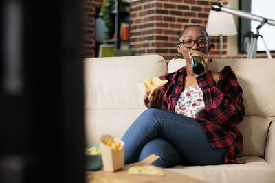 Woman drinking beer sitting on sofa at home