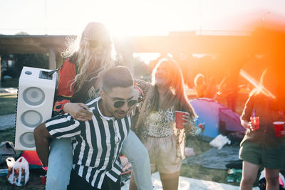 Man piggybacking female friend with speaker while enjoying in music festival