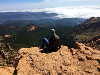 Rear view of man sitting on mountain against sky