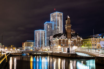 Illuminated buildings by river against sky at night