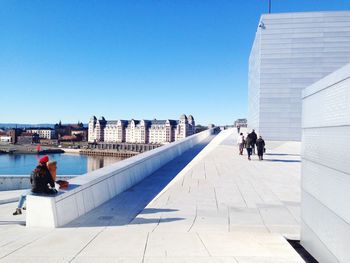 People walking on footpath by opera house against sky