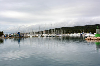 Boats in harbor against cloudy sky