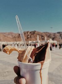 Close-up of hand holding ice cream against sky