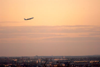 Airplane flying over cityscape against sky during sunset