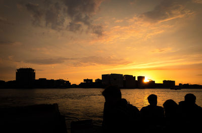 Silhouette people by river against sky during sunset
