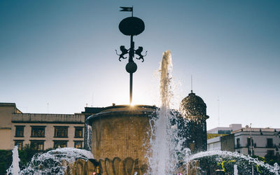 Fountain by street light against buildings in city