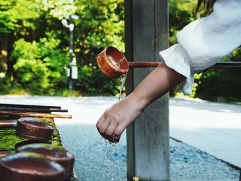 Cropped image of woman pouring water on hand with wooden ladle at temple