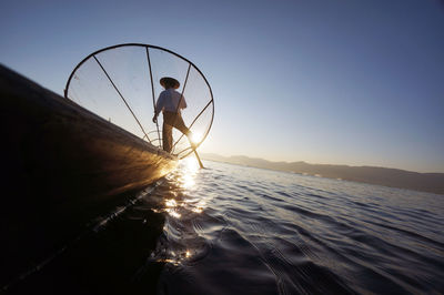 Rear view of fisherman with fishing net in boat on sea