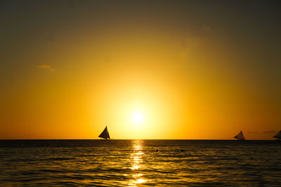 Silhouette sailboat in sea against sky during sunset