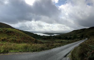 Country road along landscape against sky