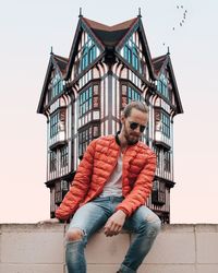 Full length of young man sitting against built structure against sky