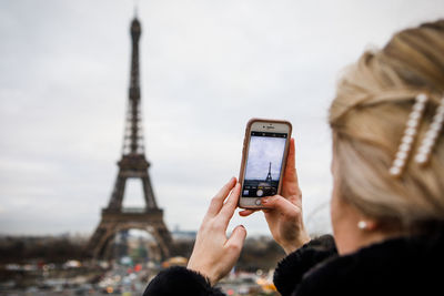 A young adult takes an iphone picture of the eiffel tower in paris.