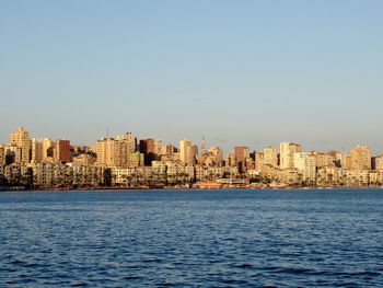 Sea by buildings in city against clear sky