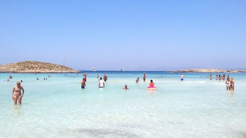 People swimming in sea against clear blue sky