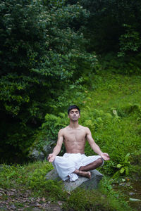 Full length of young man meditating while sitting on rock