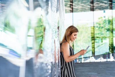 Side view of a beautiful girl using smartphone while leaning on a wall